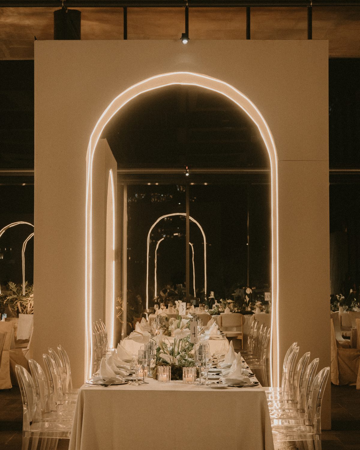 Una mesa larga bajo un arco delineado con luz, con más arcos iluminados al fondo del salón a oscuras.